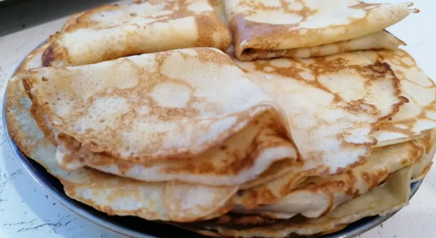 Stos cienkich, złocistych naleśników, idealnych na śniadanie lub deser. Każdy z nich ma delikatne pęcherzyki i lekko przypieczone brzegi.
