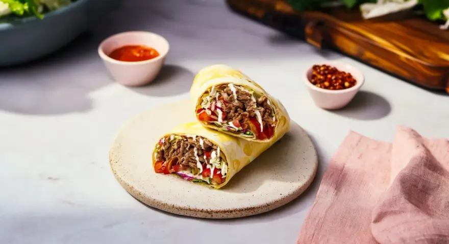 Pyszny rollo z mięsem, warzywami i sosem, podany na talerzu. Obok miseczki z sosem i papryczkami chili.