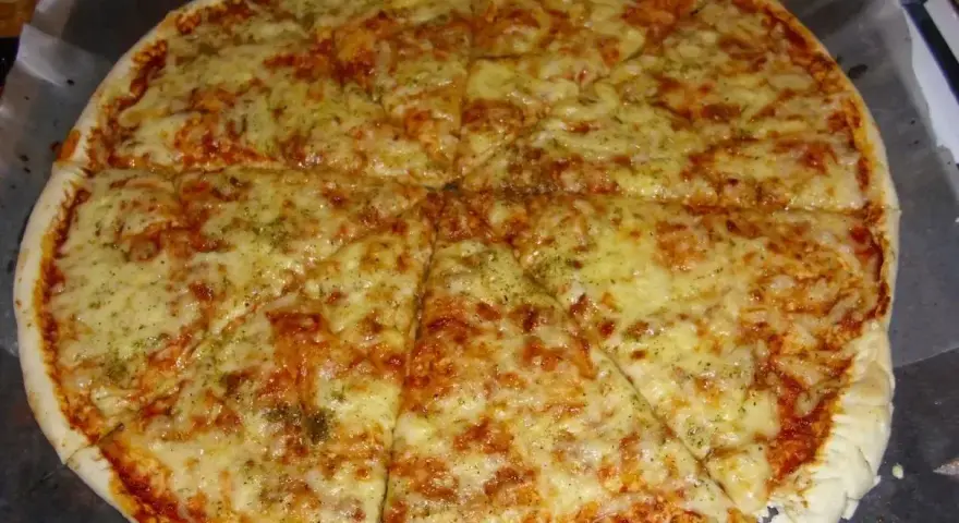 Pyszna pizza margerita z ciągnącym się serem i aromatycznymi ziołami, pokrojona na 8 kawałków.