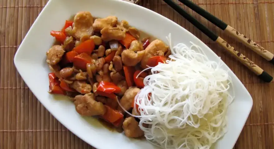 Kurczak kung pao po seczuańsku z orzeszkami ziemnymi i papryką, podany z ryżowym makaronem.