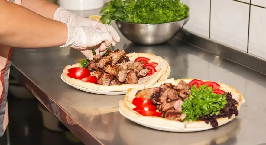 Ręce w rękawiczkach układają mięso na plackach z pomidorami i zieloną sałatą. Pyszny kebab gemuse gotowy do podania.