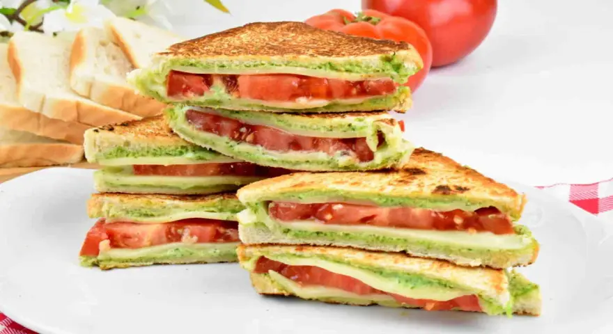 Pyszne włoskie kanapki z pomidorami i zielonym pesto, ułożone na talerzu. Idealne na lekki posiłek.