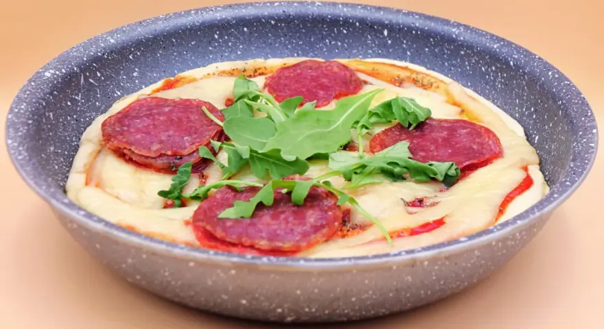 Mini pizza na patelni z serem, rukolą i plasterkami pikantnej salsiccii.