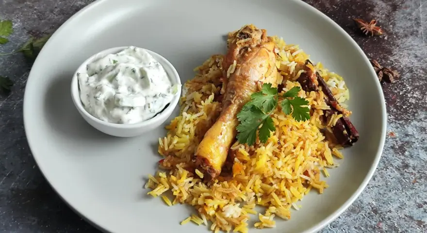 Pyszny kurczak biryani z ryżem, jogurtowym dipem i przyprawami.