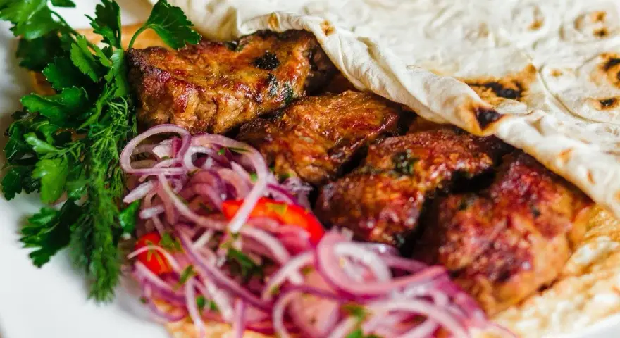 Pyszne mezze: soczyste mięso zawinięte w placek, z dodatkiem świeżej natki i czerwonej cebuli. Idealne na przekąskę.