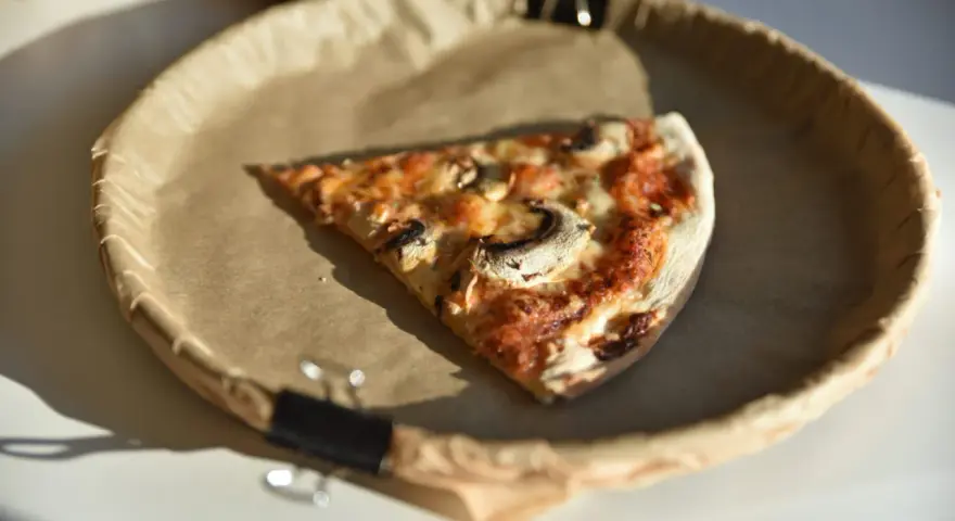 Kawałek pizzy z pieczarkami na papierowym talerzu. Zastanawiasz się, ile kalorii ma pizza?