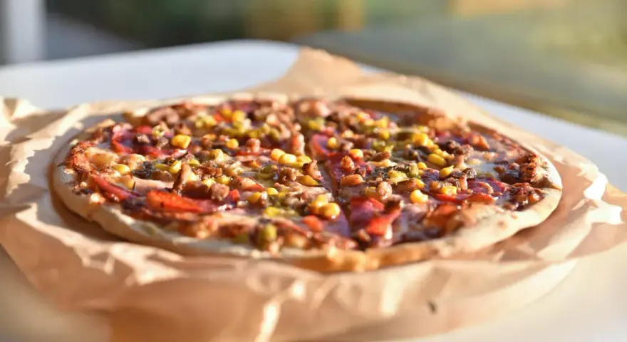 Apetyczna pizza Guiseppe 4 sery, z widocznymi kawałkami mięsa, kukurydzy i papryki, leży na papierze do pieczenia.