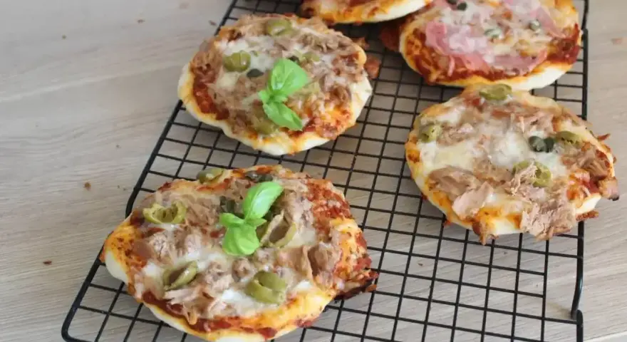 Kilka pysznych pizzett z tuńczykiem, oliwkami i bazylią na czarnej kratce.