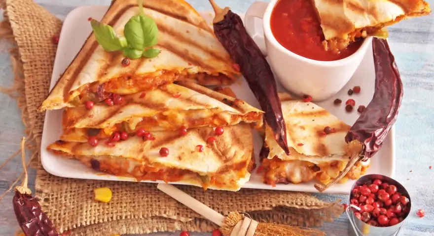 Pyszna quesadilla z serem i papryczkami chili, podana z sosem pomidorowym i ziarnami pieprzu.