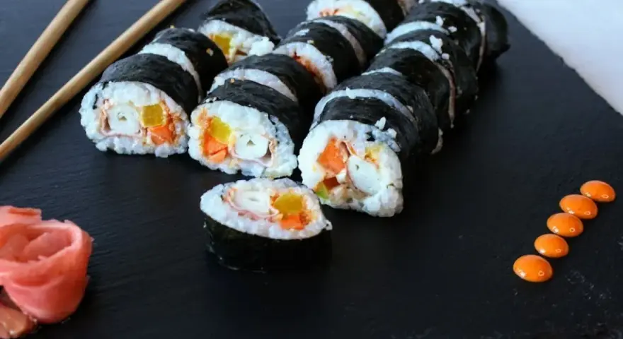 Rząd hosomaki surimi z marchewką i żółtą papryką, podane z imbirem i pomarańczowym sosem.