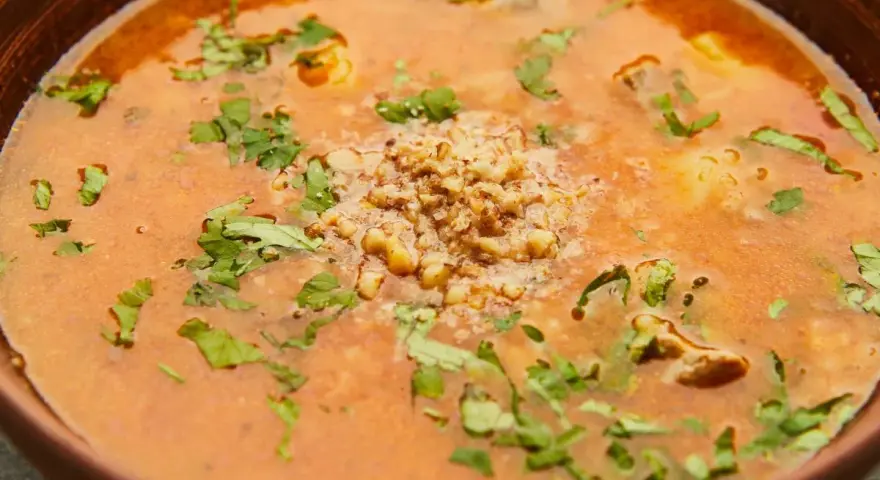 Aromatic gruzińska zupa charczo w glinianej misce, ozdobiona posiekanymi orzechami i świeżą kolendrą.