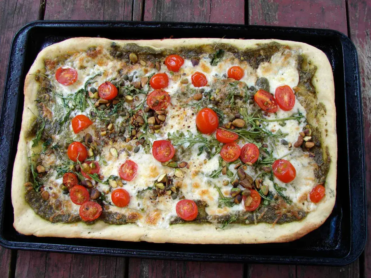 Prostokątna pizza z zielonym pesto, pomidorkami koktajlowymi, pistacjami i rukolą. Idealna na letnie popołudnie, smakuje jak prawdziwa spinata!