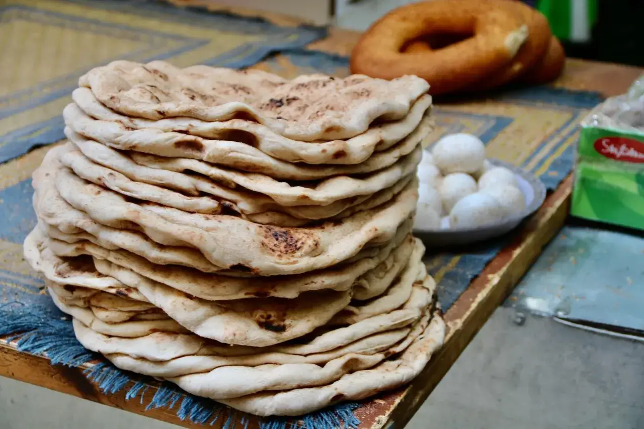 Stos świeżego, ciepłego ciasta na kebab, obok miseczki z jajkami i okrągłego chleba.