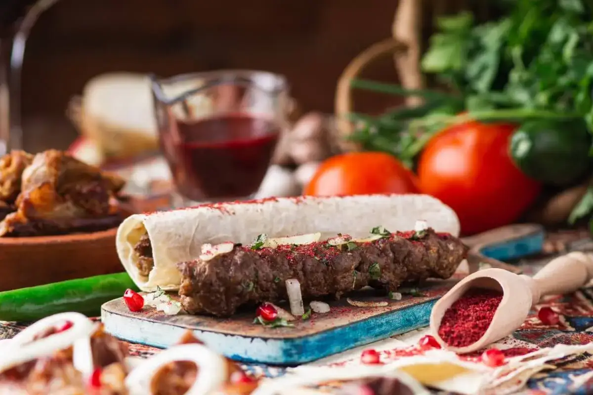 Pyszny gruziński kebab zawinięty w lawasz, posypany sumakiem i ziołami, z dodatkami warzyw i sosu.