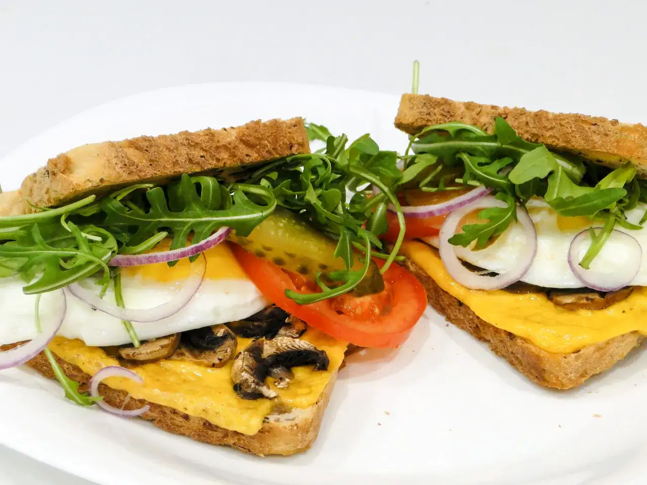 Dwa pyszne croque madame z jajkiem sadzonym, serem, rukolą, pomidorem i pieczarkami na chrupiącym toście.