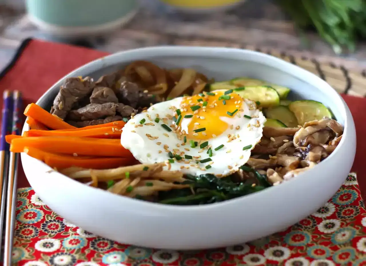 Apetyczny bibimpap z wołowiną, warzywami i jajkiem sadzonym, posypany sezamem i szczypiorkiem.