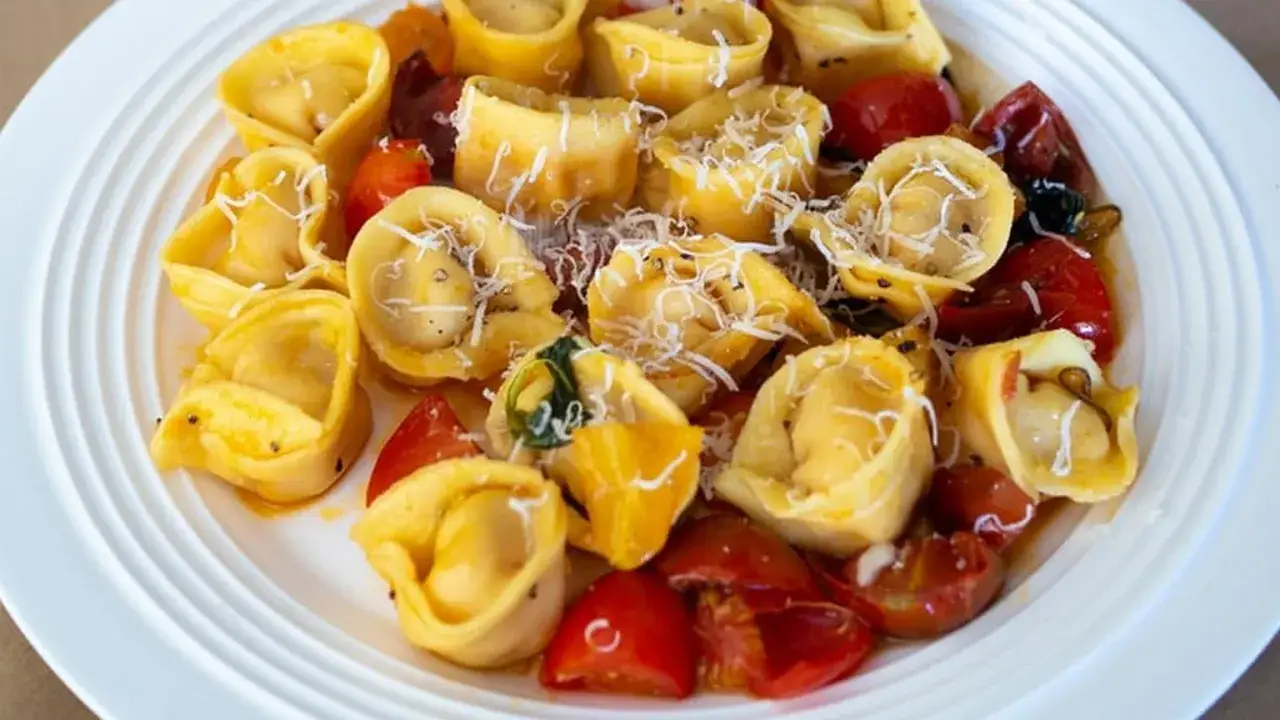 Pyszne raviolini z pomidorkami koktajlowymi i parmezanem, podane na białym talerzu.