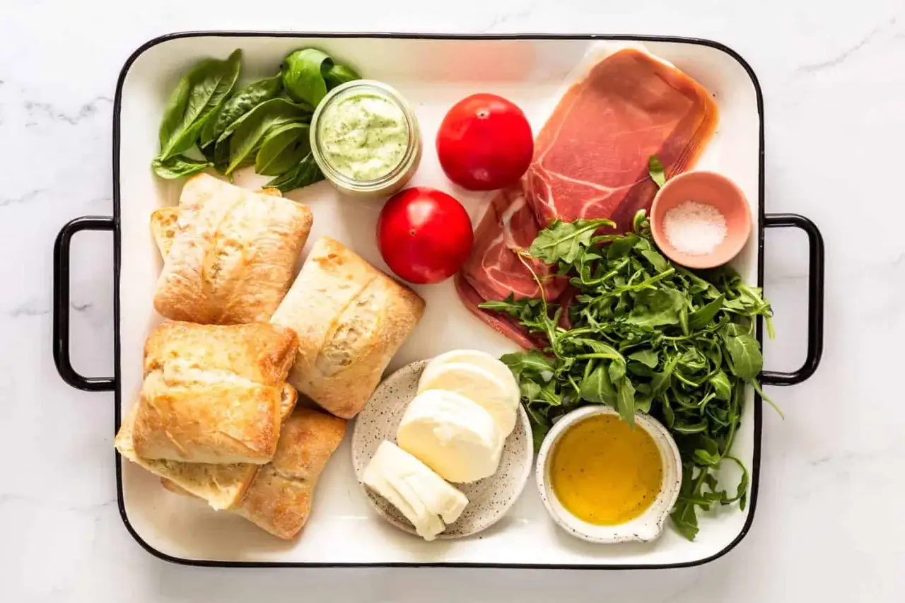 Składniki na pyszne panini: bułki, prosciutto, mozzarella, pomidory, rukola, bazylia, sos i oliwa.