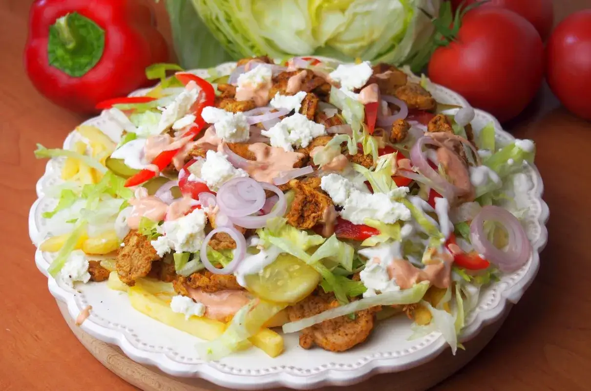 Kebab z frytkami belgijskimi, sałatą, serem feta, pomidorami i sosem. Pyszne danie na talerzu.