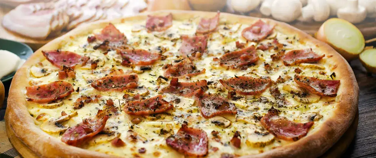 Pizza z chrupiącym guancialle, grzybami i cebulą, posypana ziołami.