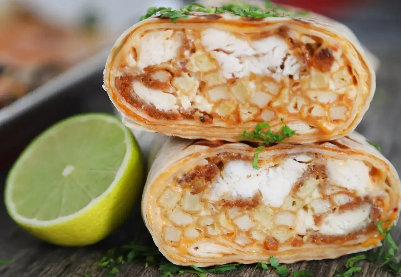 Pyszne french tacos z kurczakiem, frytkami i sosem, ozdobione natką pietruszki. Obok połówka limonki.