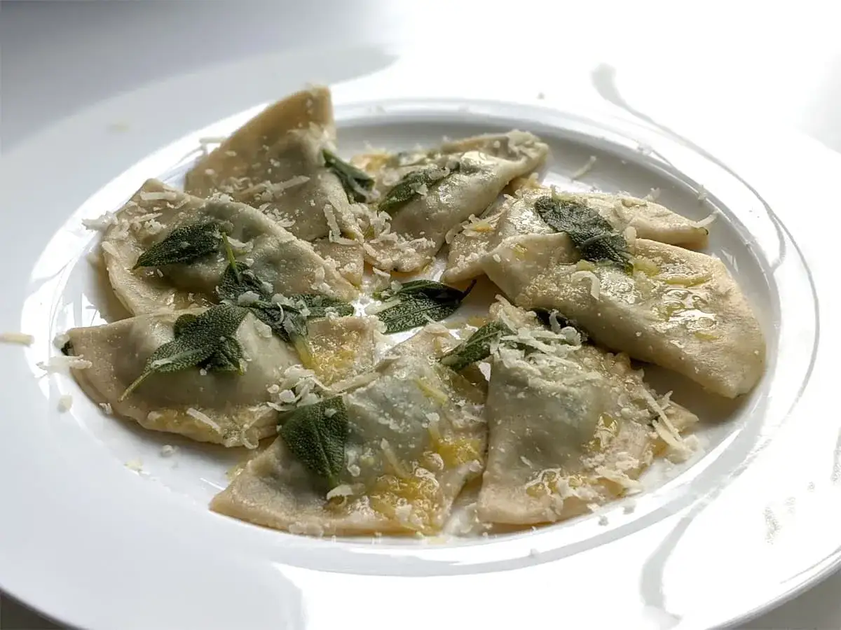 Ravioli z czym podawać? Pyszne ravioli z szałwią, masłem i parmezanem na białym talerzu.