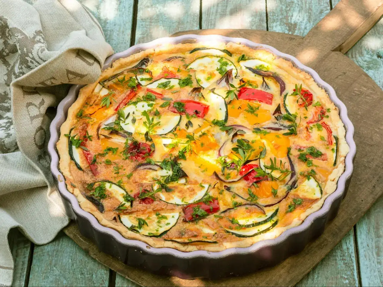 Pyszny, kolorowy kisz z cukinią, papryką i cebulą, posypany świeżą natką pietruszki.