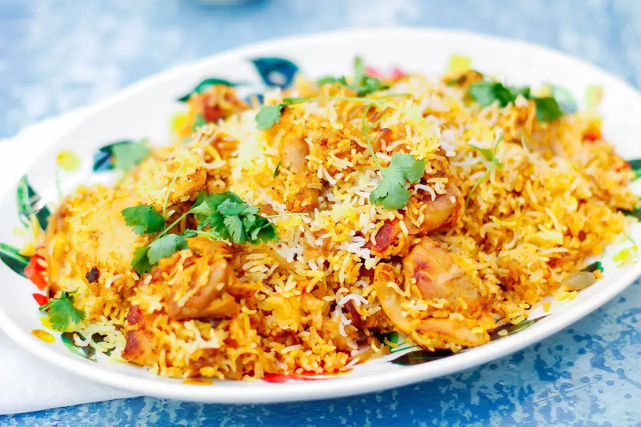 Pyszny kurczak biryani, aromatyczny ryż z kawałkami kurczaka, udekorowany świeżą kolendrą, podany na talerzu z motywem liści.