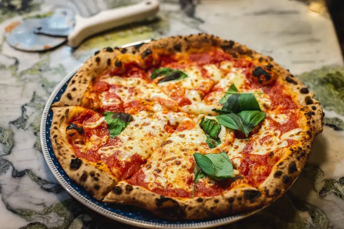 Pyszna pizza margerita z rozpływającym się serem, sosem pomidorowym i świeżą bazylią, gotowa do pokrojenia.