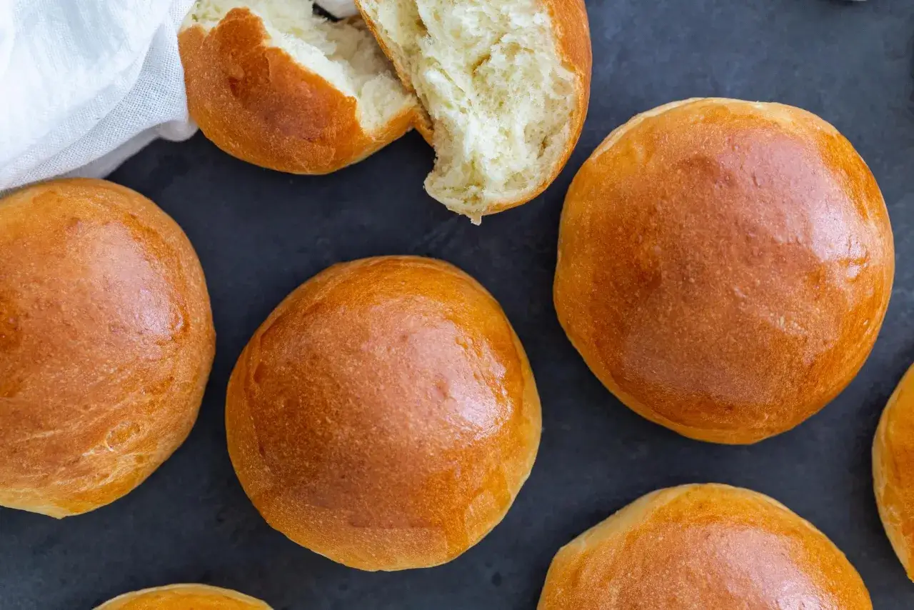 Złociste, puszyste bułki brioche, jedna przekrojona, ukazująca miękki środek. Idealne na słodkie i wytrawne śniadanie.