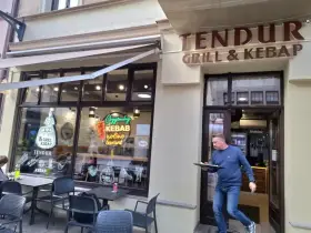 Mężczyzna wychodzi z lokalu "Tendur Grill & Kebap", niosąc talerz. W witrynie neonowy napis "Oryginalny Kebab".