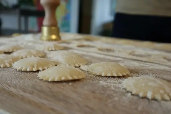 Świeże ravioli na drewnianej desce, posypane mąką. Zastanawiasz się, ravioli z czym podawać?