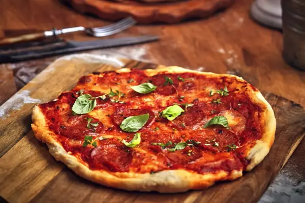 Pikantna spianata calabrese na pizzy, ozdobiona świeżą bazylią i ziołami, czeka na talerzu.