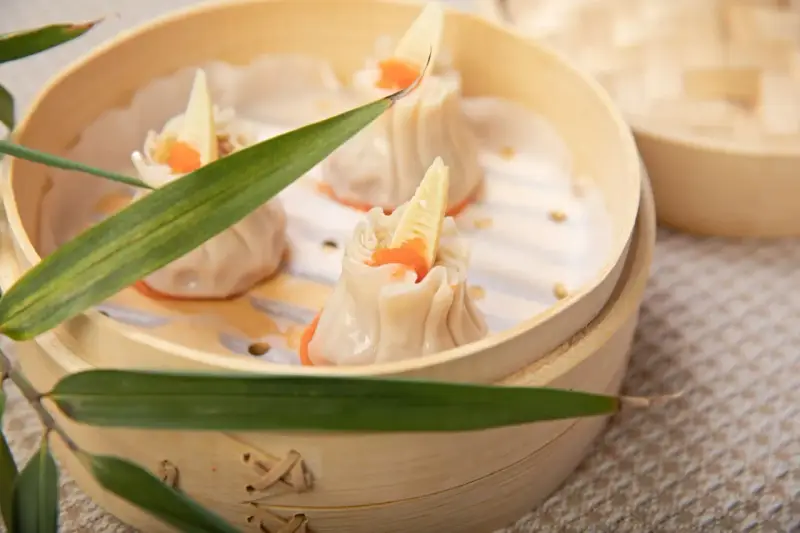 Pierożki dim sum w bambusowym parowniku, ozdobione kawałkiem bambusa i pomarańczowym ikrą.
