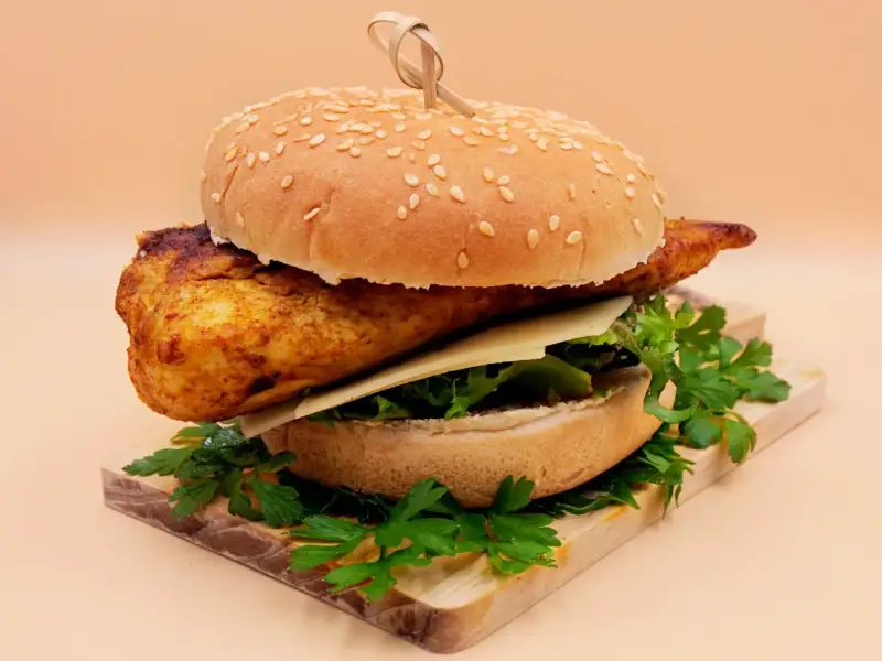 Pikantny kurczakburger z serem i świeżą sałatą, podany na desce z natką pietruszki.