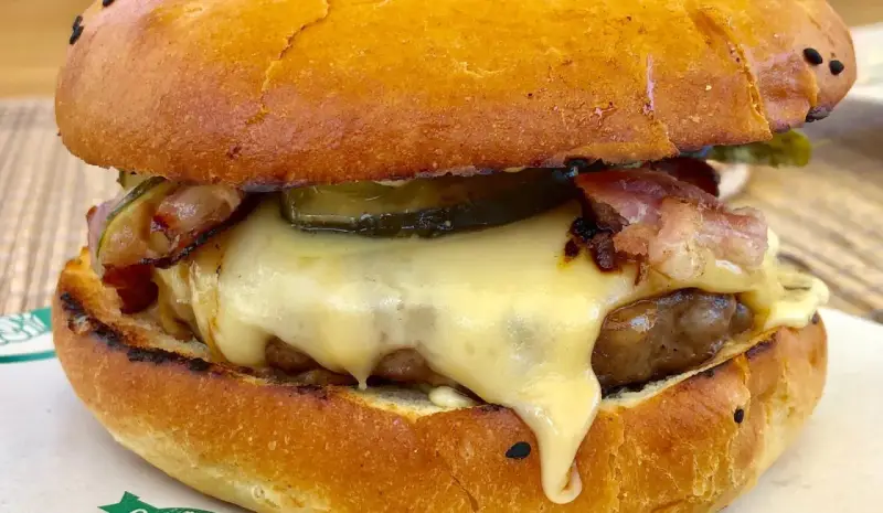 Pyszny burger z dzika z rozpływającym się serem, chrupiącym boczkiem i piklami. Idealny na leśną ucztę!