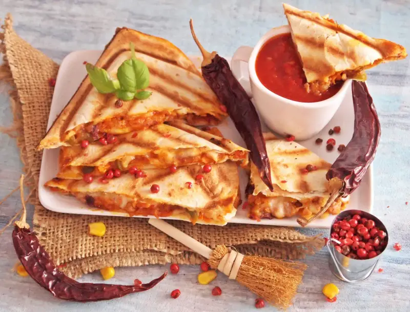 Pyszna quesadilla z serem i papryczkami chili, podana z sosem pomidorowym i ziarnami pieprzu.